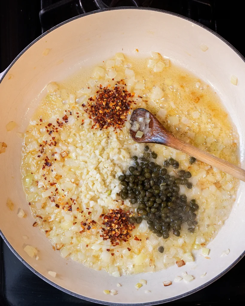 Add capers, crushed red pepper, and garlic to onion